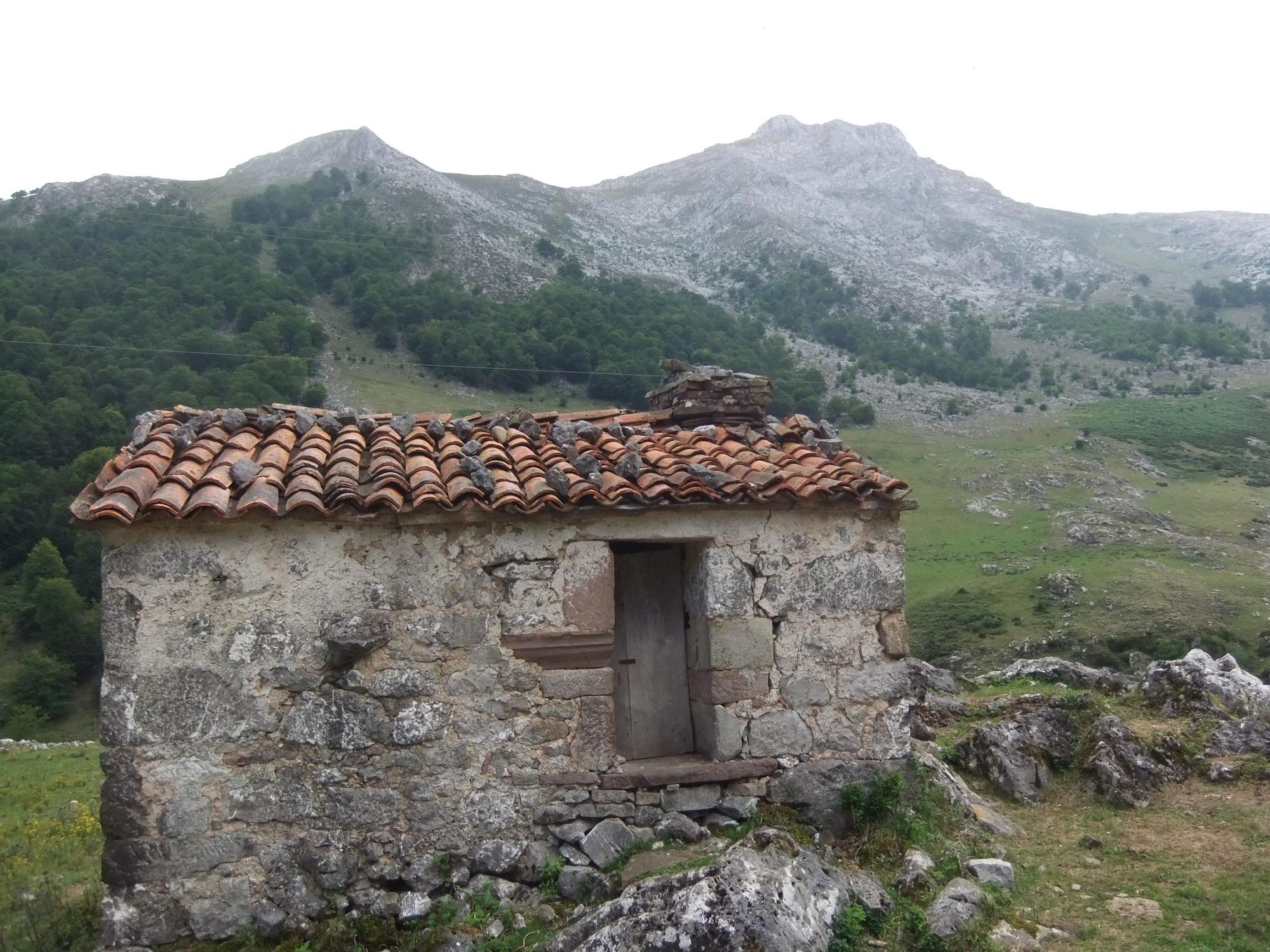 Cabaña en la majada de Sahugu, con restos de la antigua capilla. Al fondo, el Canto Cabroneru.