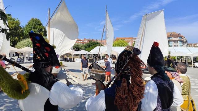 Unos gaiteiros animan la fiesta con las embarcaciones tradicionales al fondo.