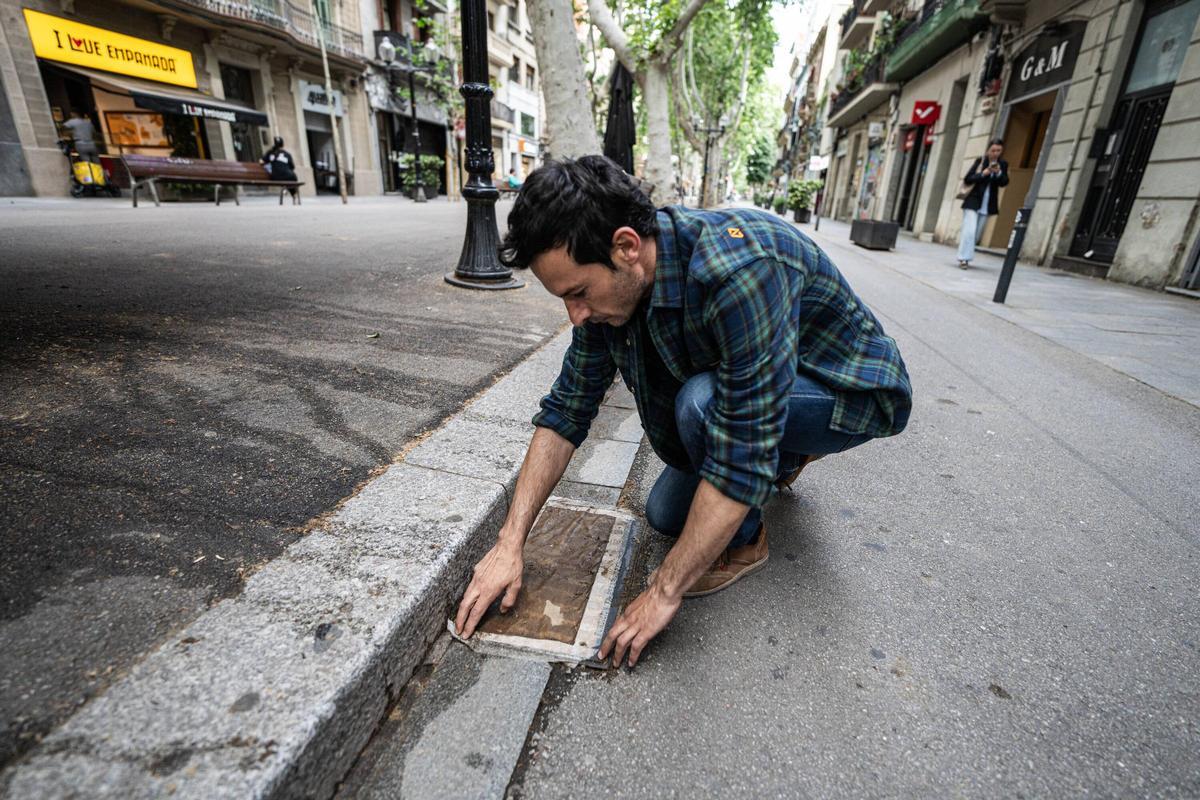 Xavi Ventura, comerciante del Poblenou, revisa la lámina con la que cubre la tapa de alcantarilla frente a su tienda para evitar malos olores, en Barcelona.