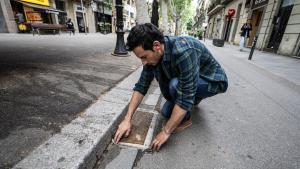 Xavi Ventura, comerciante del Poblenou, revisa la lámina con la que cubre la tapa de alcantarilla frente a su tienda para evitar malos olores, en Barcelona.