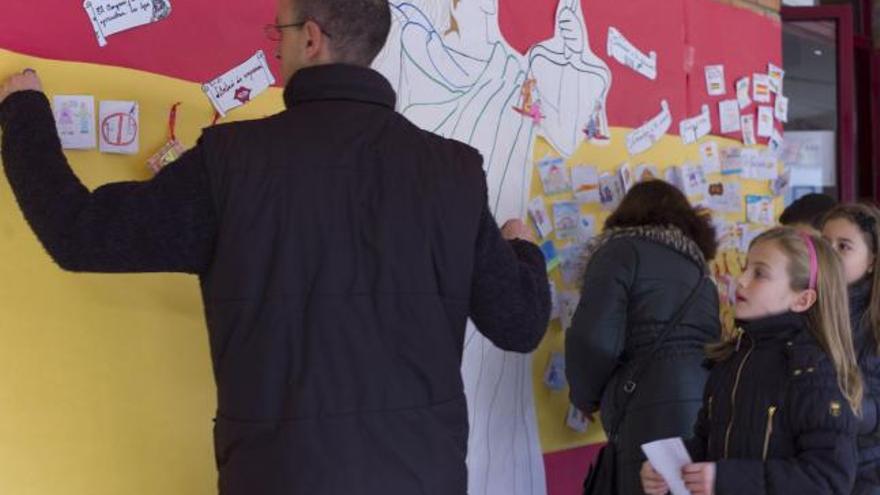 Un profesor ayuda a pegar los artículos de los alumnos en el mural.