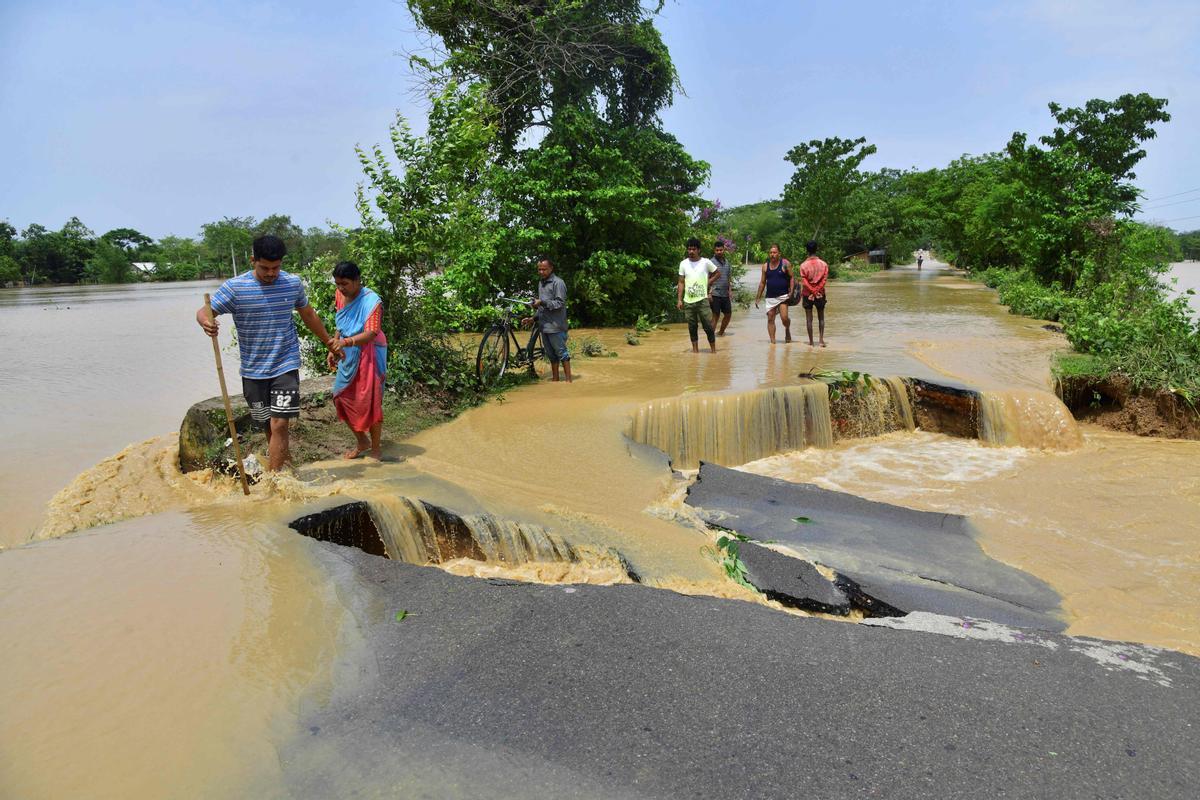 Un grupo de gente trata de cruzar una carretera seriamente dañada por las inundaciones tras las intensas lluvias en el distrito de Nagaon, en el estado de Assam, en India, el 19 de mayo del 2022.