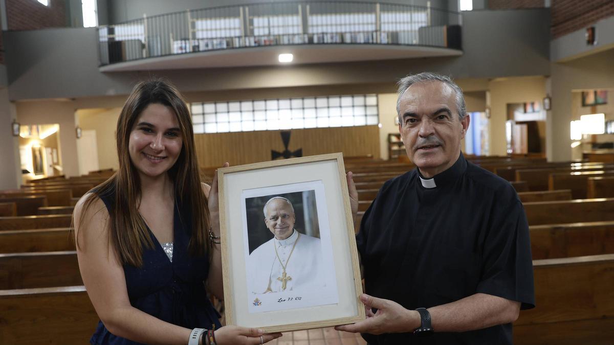Lourdes Peralta sostiene un retrato de León XIV con el párroco de Ventanielles, Jaime Sanz Santacruz.