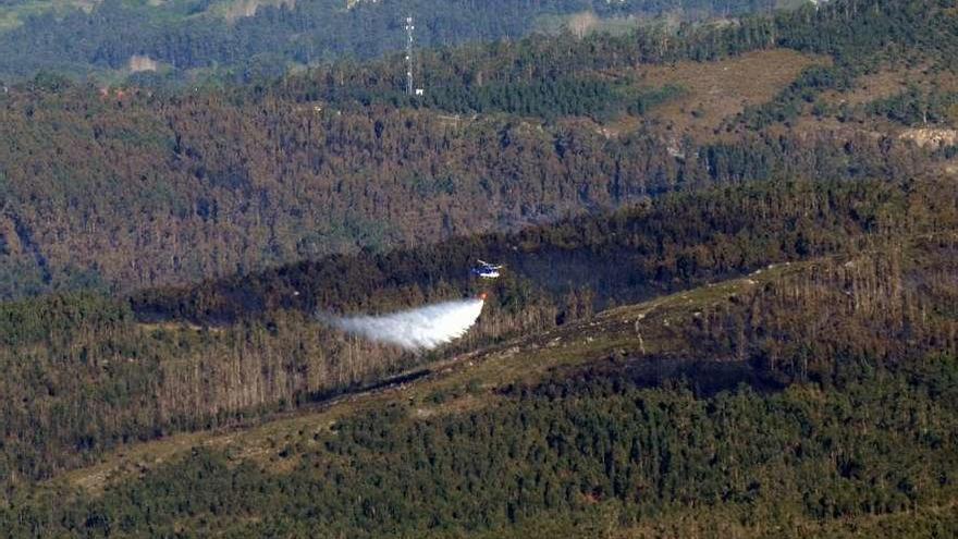 Un helicóptero refresca el monte quemado en Rianxo. // Noé Parga