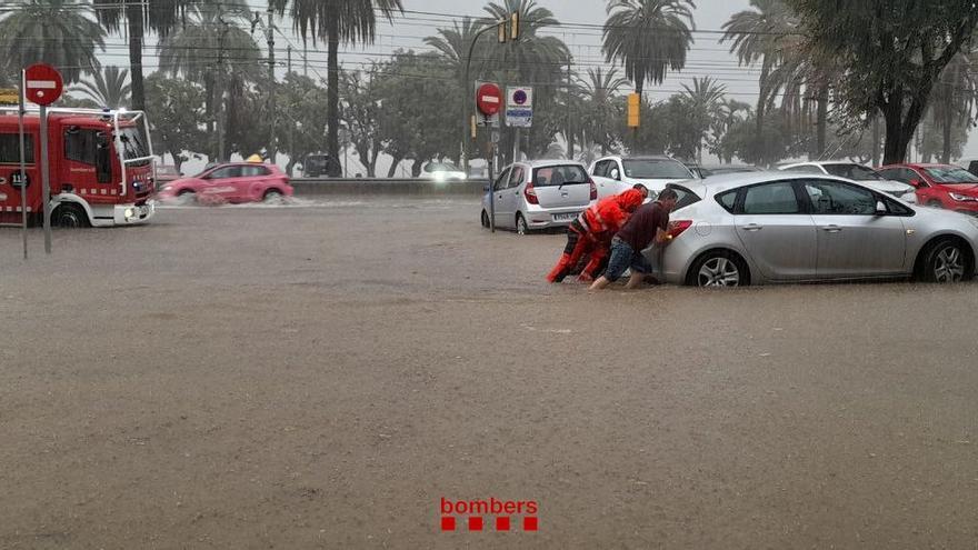 Efectius dels Bombers ajuden un home a empènyer un cotxe encallat per la pluja