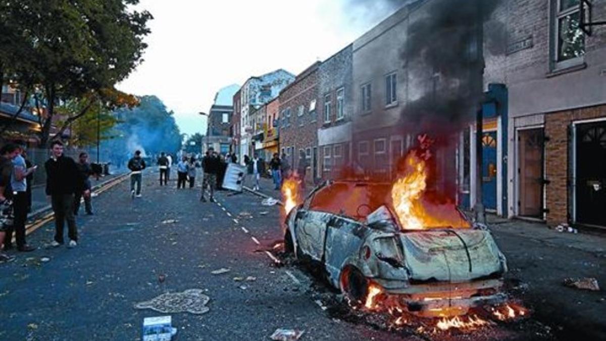 Un coche incendiado  por jóvenes en una calle del barrio de Hackney, el pasado lunes.