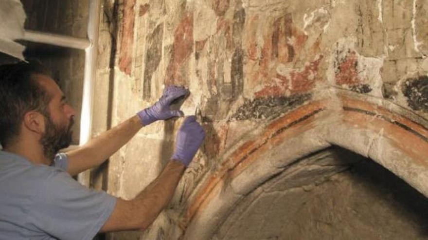 Uno de los restauradores intenta consolidar una parte de las pinturas del muro junto a la torre de la iglesia.