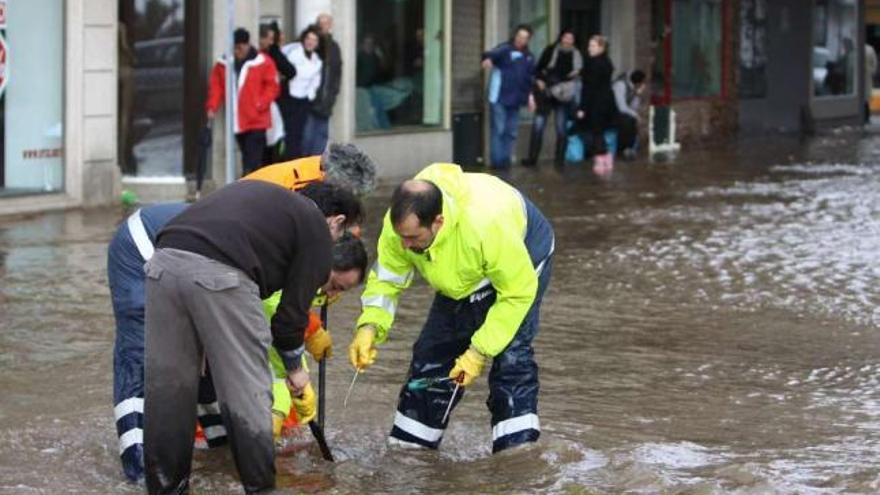 Operarios y vecinos, ayer, trabajando en una alcantarilla en una calle anegada del centro de Cangas. / c. giménez