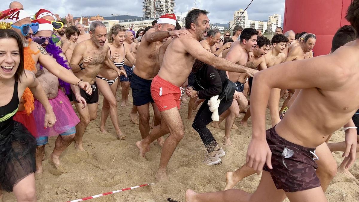 Bañistas entrando al agua durante el primer baño del año en la playa de Mataró