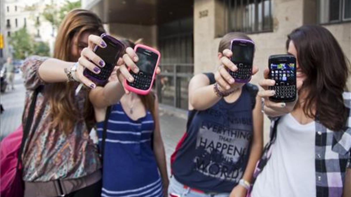 Unas adolescentes muestran sus teléfonos móviles a la puerta de su instituto en Barcelona