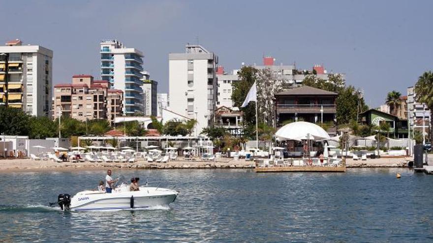 Una barca navega por el puerto de Gandia, frente al chiringuito «chill out» habilitado en el antiguo varadero, al fondo.