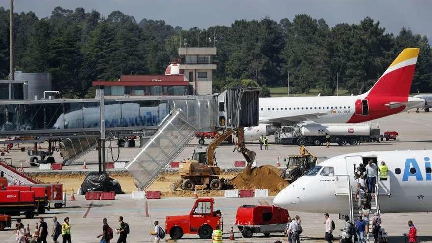 Pasajeros pasan delante de las obras en el estacionamiento de aviones en Peinador. // J. Lores