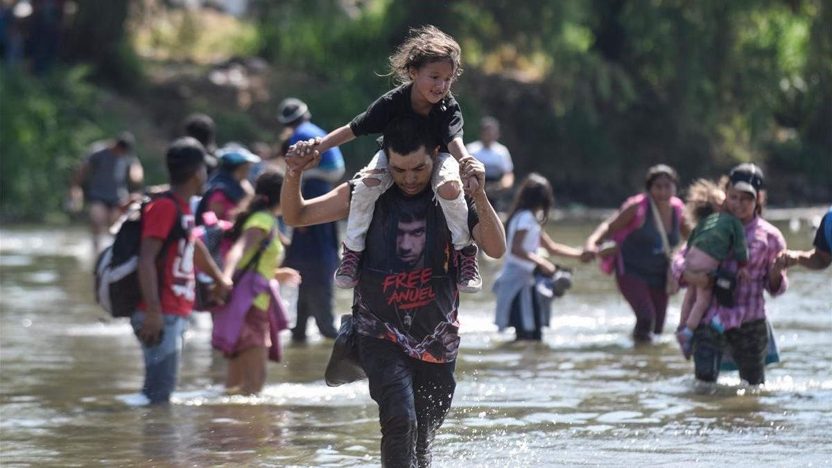 Varios migrantes cruzan el río Suchiate con sus hijos en brazos.