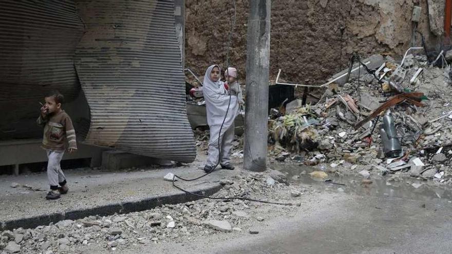 Dos niños, una con un bebé en brazos, caminan entre ruinas en las afueras de Damasco. // Reuters
