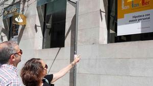 Una pareja viendo un anuncio de una hipoteca en la cristalera de un banco en Vigo.