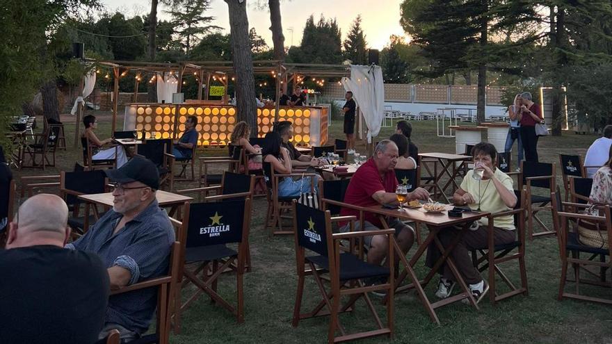 Assistents al primer esdeveniment gaudint del vespreig, amb l'autobús del DJ i la foodtruck al fons