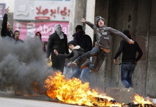 A Palestinian youth throws a stone towards Israeli soldiers as he jumps over burning tyres during clashes that followed a rally to support President Mahmoud Abbas in the West Bank city of Hebron