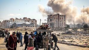 Palestinos huyen de Jan Yunis, en la Franja de Gaza, mientras, al fondo, se aprecia el humo de un bombardeo.