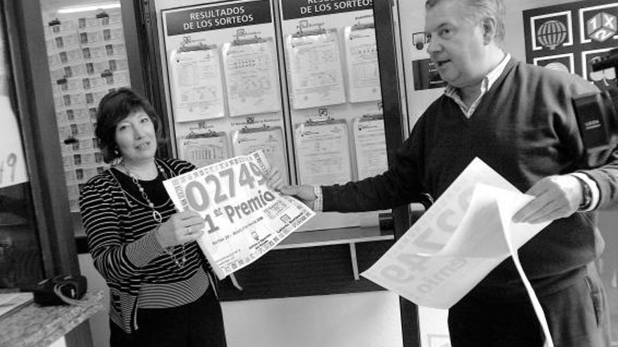 Un representante de Loterías del Estado entrega a Amelia García el cartel del premio en su administración.