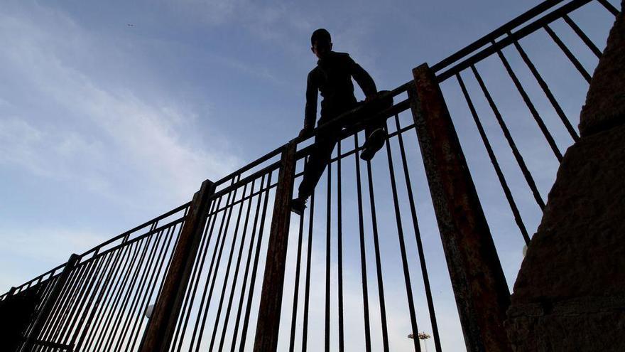 Un joven marroquí intenta saltar la verja del puerto de Melilla.  // AFP