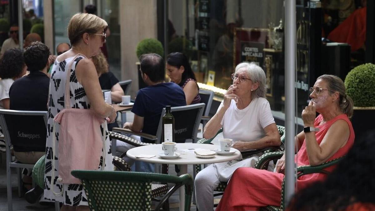Dos señoras conversan con una tercera mientras fuman en una terraza.