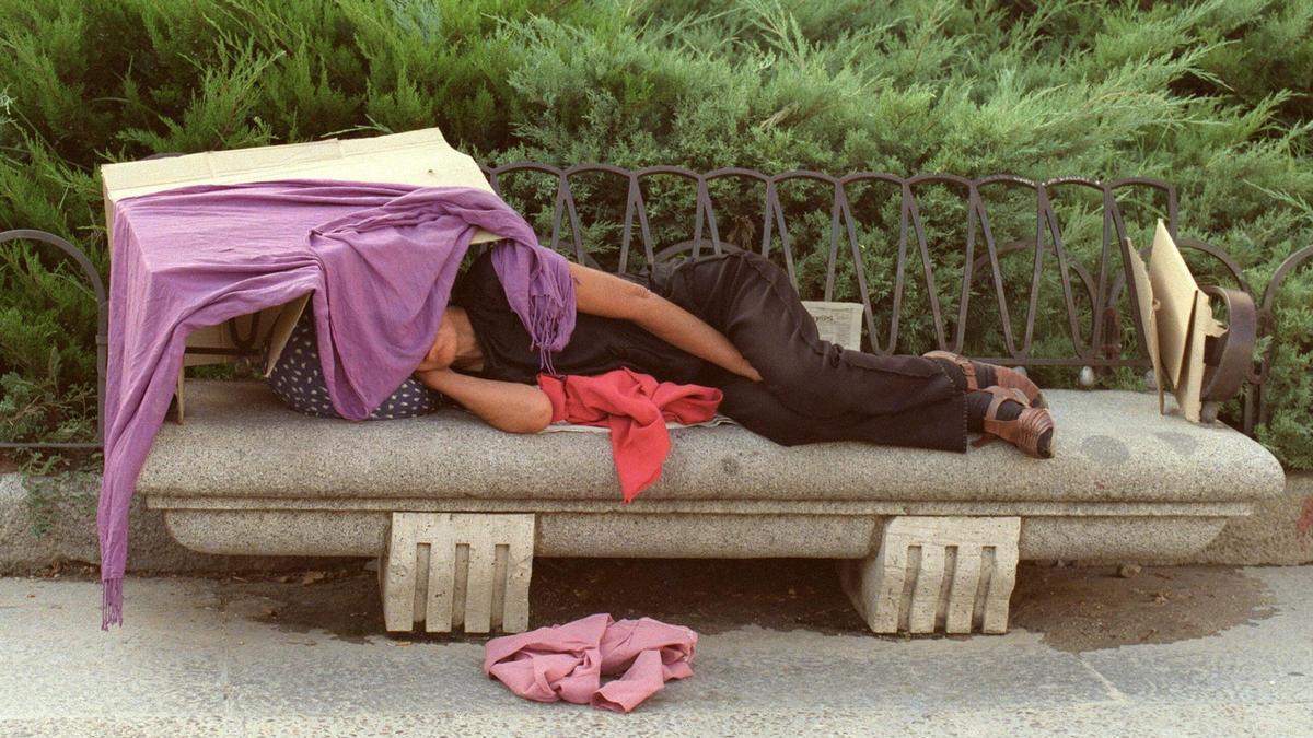 Una indigente duerme en el banco de un parque de Madrid.