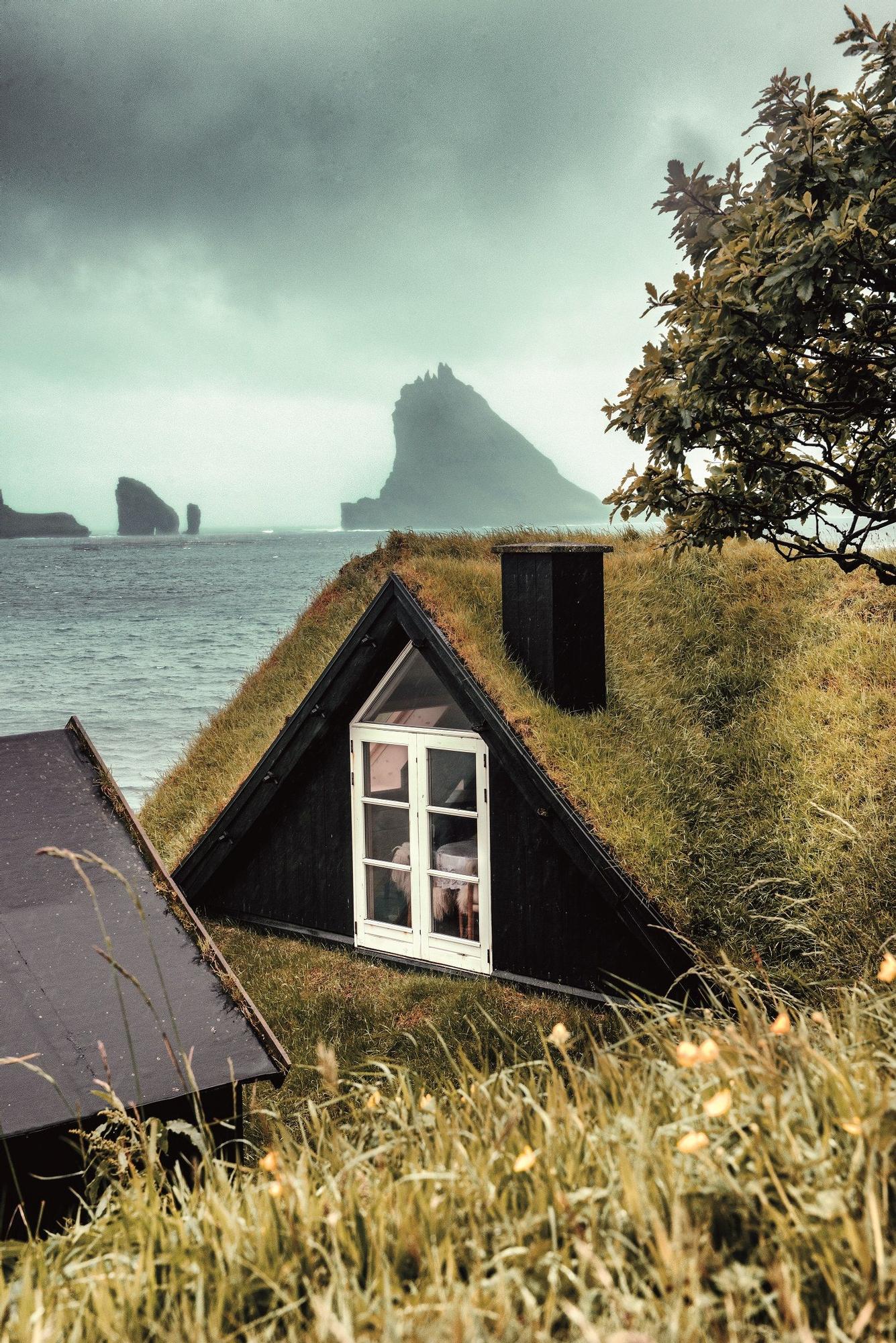 Tejado tradicional con hierba y vistas del islote de Tindhólmur al fondo.