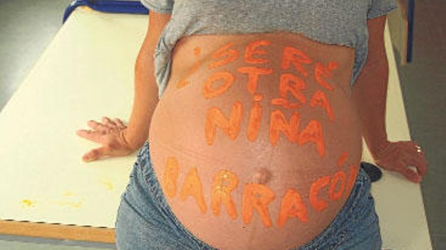 La madre muestra el vientre con una de las frases, apoyada en una mesa del colegio.