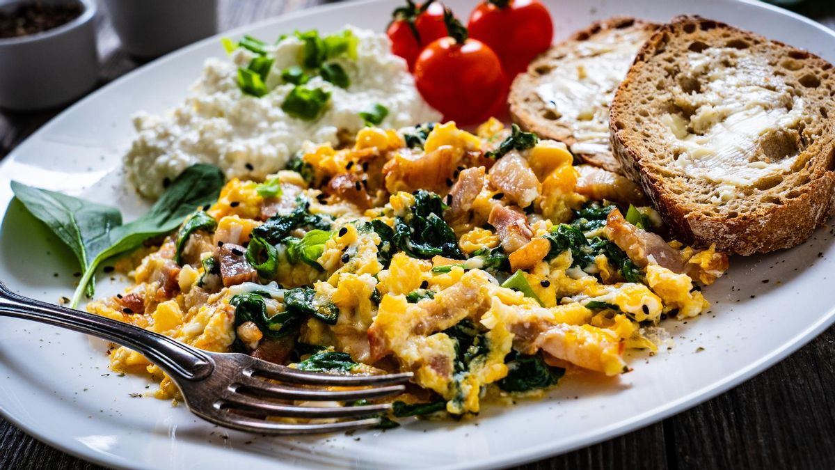 Un plato de huevos revueltos con verduras, queso, tomate y tostadas.