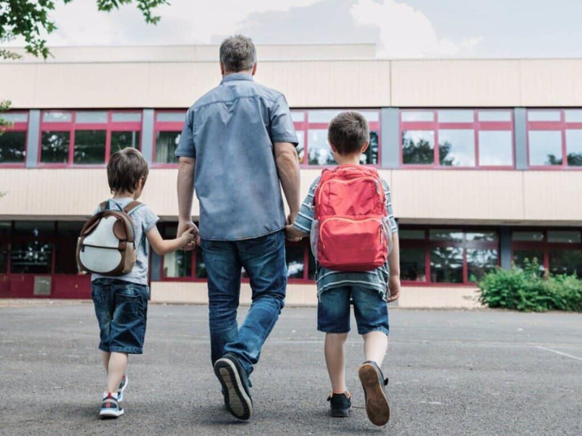 Un padre, con sus dos hijos, a la entrada de un colegio en el primer día de la vuelta al cole tras las vacaciones de verano