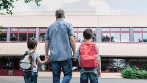 Un padre, con sus dos hijos, a la entrada de un colegio en el primer día de la vuelta al cole tras las vacaciones de verano
