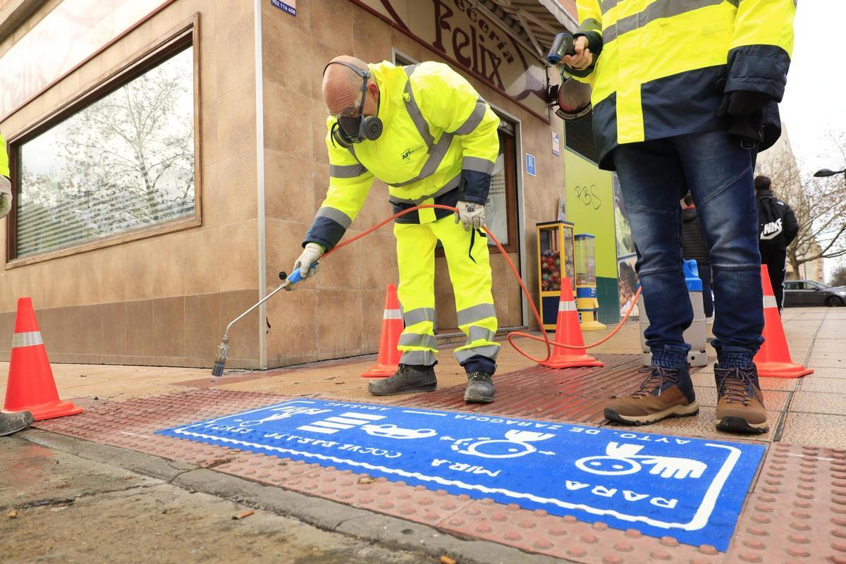 Un operario pinta en el suelo las nuevas señales de advertencia en el entorno de los colegios.