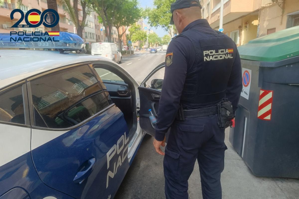 Un agente de la Policia Nacional en Palma junto al coche patrulla.