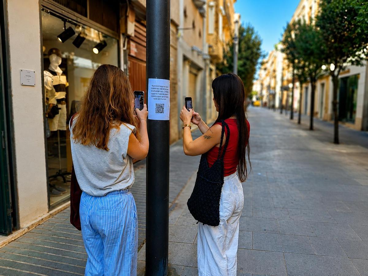 Almudena Blanco y Beatriz Moñino escanean el código QR de uno de los carteles en la calle Menacho.