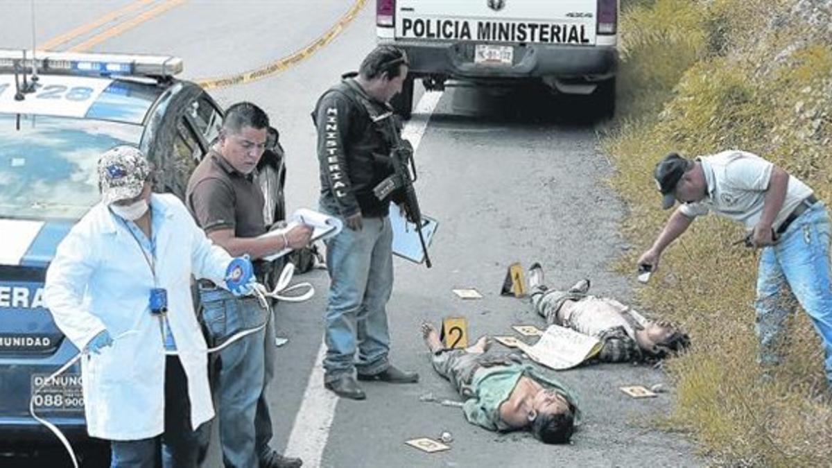 Unos agentes inspeccionan dos cadáveres en la autopista hacia Iguala, en el estado de Guerrero.