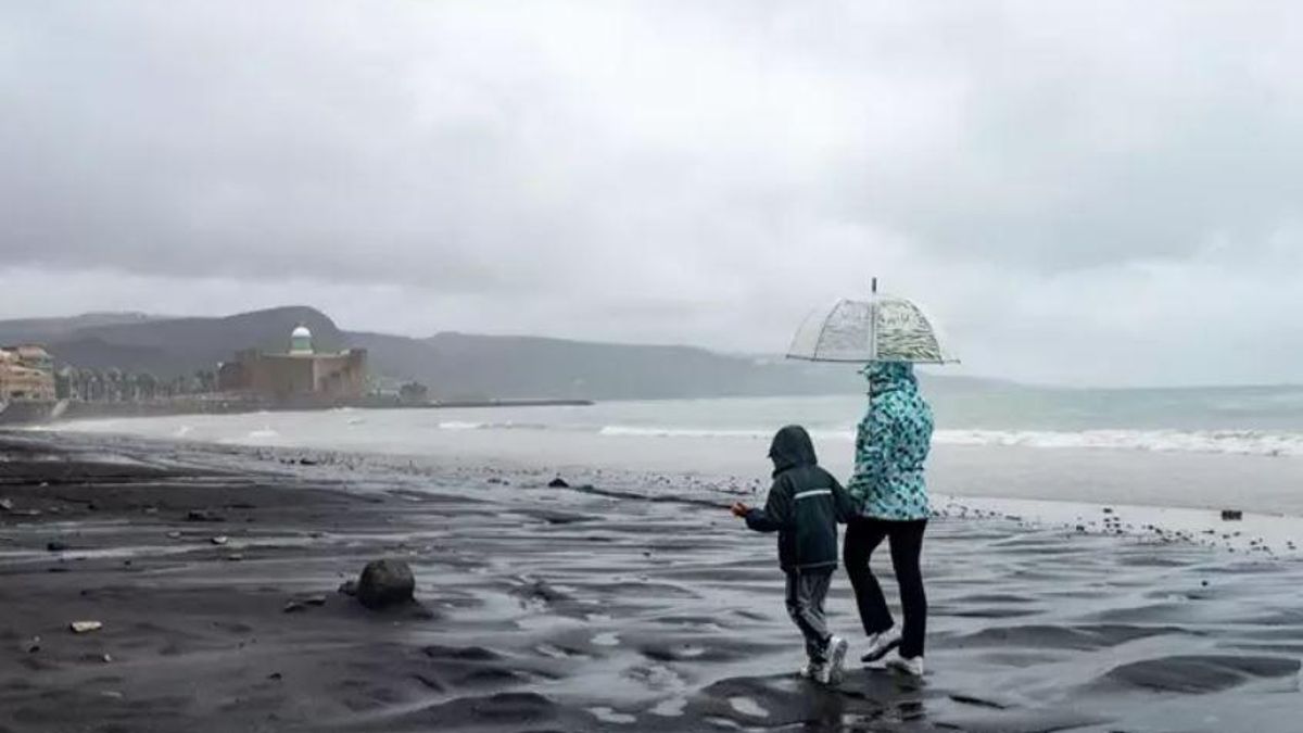 Dos personas se cubren de la lluvia con un paraguas mientras caminan por una playa en Las Palmas de Gran Canaria, Canarias (España)