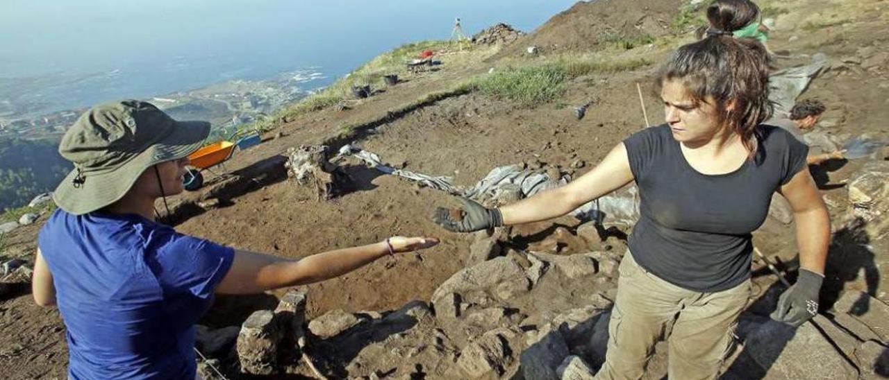 Dos arqueólogas recogen una pieza hallada en la reciente excavación de A Cabeciña. // Marta G. Brea