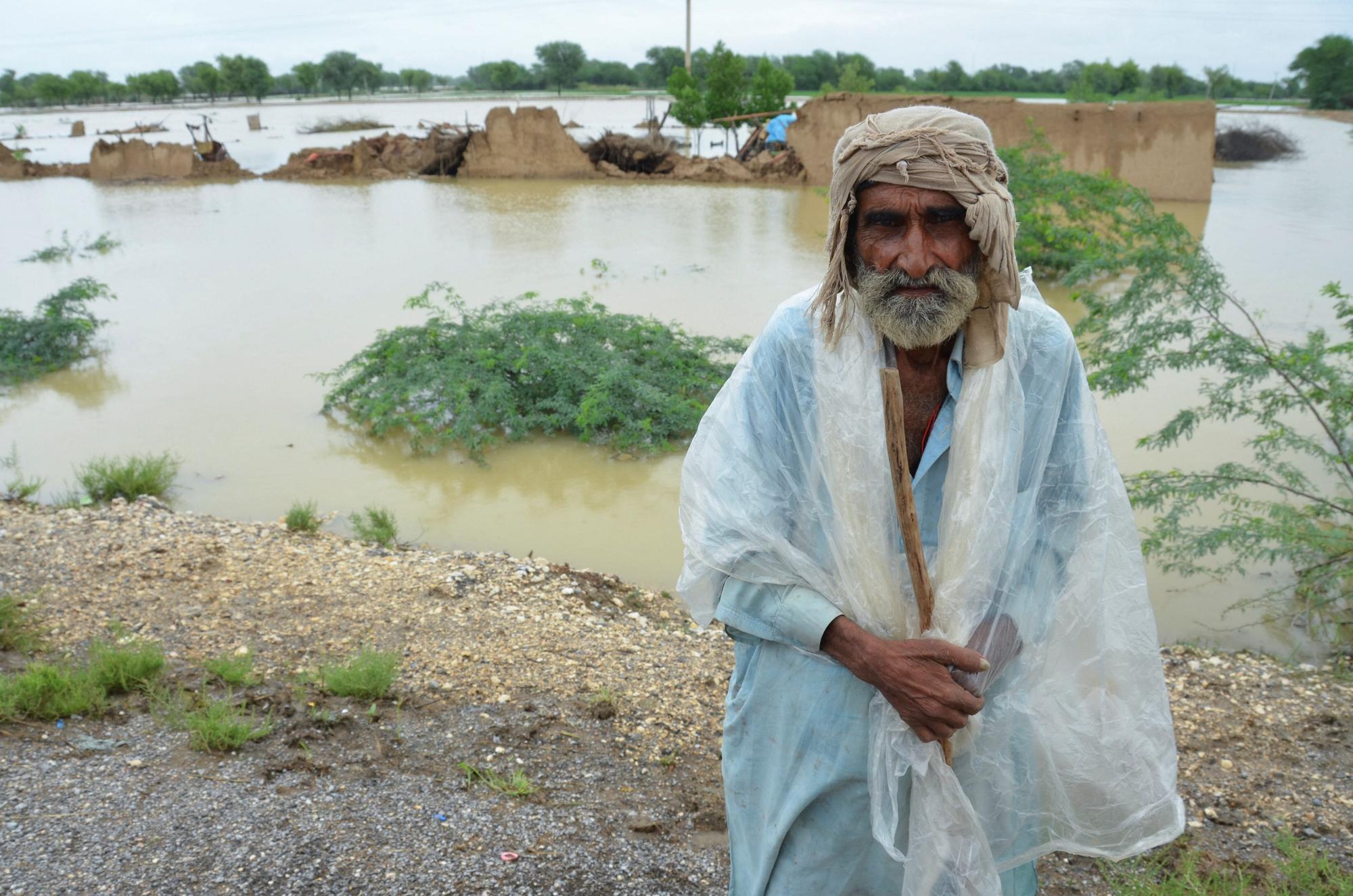 A flood victim covers himself with a plastic sheet to avoid rain, with damaged houses in the background, following rains and floods during the monsoon season in Jafarabd,