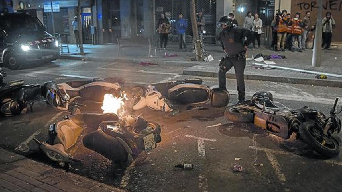 Un antidisturbios observa motos afectadas por los actos vandálicos durante las protestas en Gràcia contra el desalojo del 'banc expropiat'.