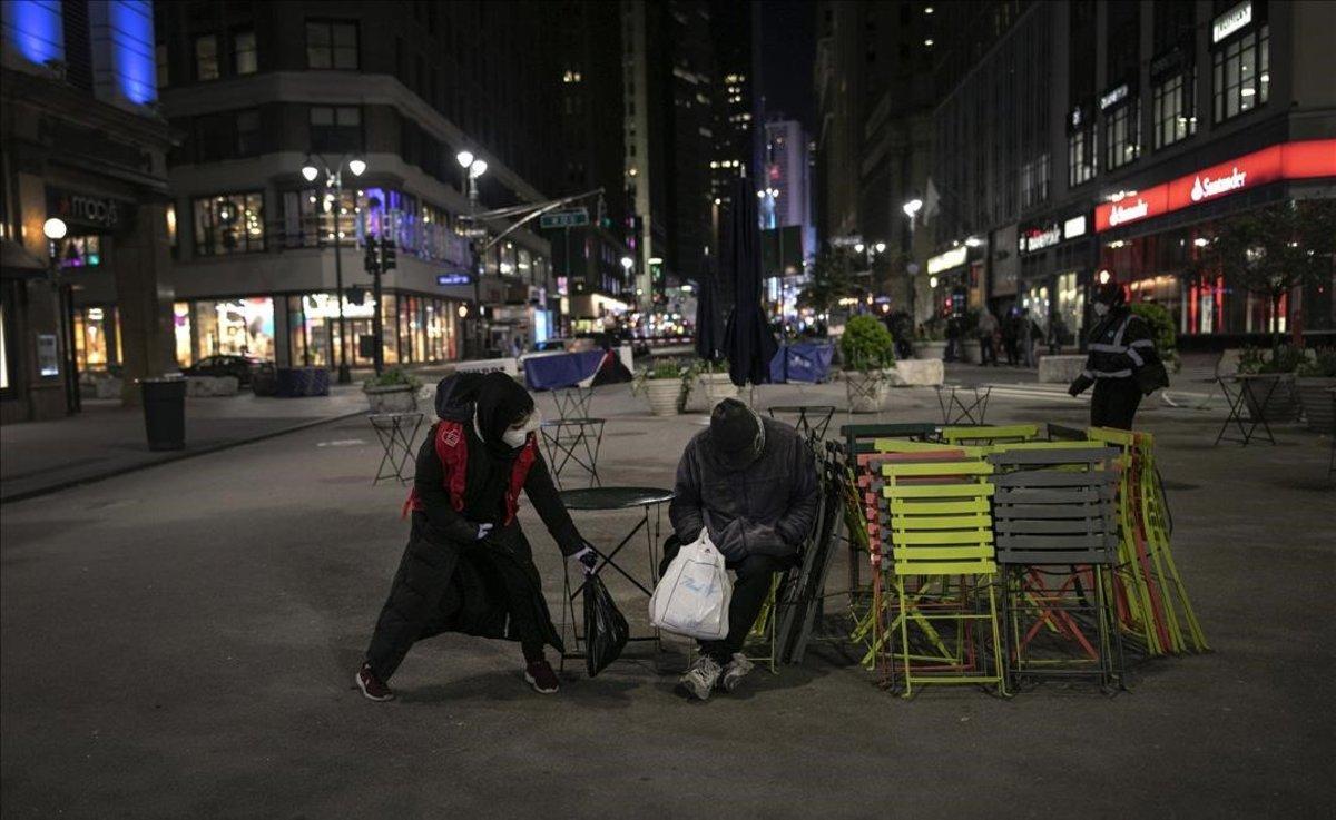 Una voluntaria deposita un paquete de comida caliente junto a un hombre sin hogar, en la plaza de Herald, de Nueva York.