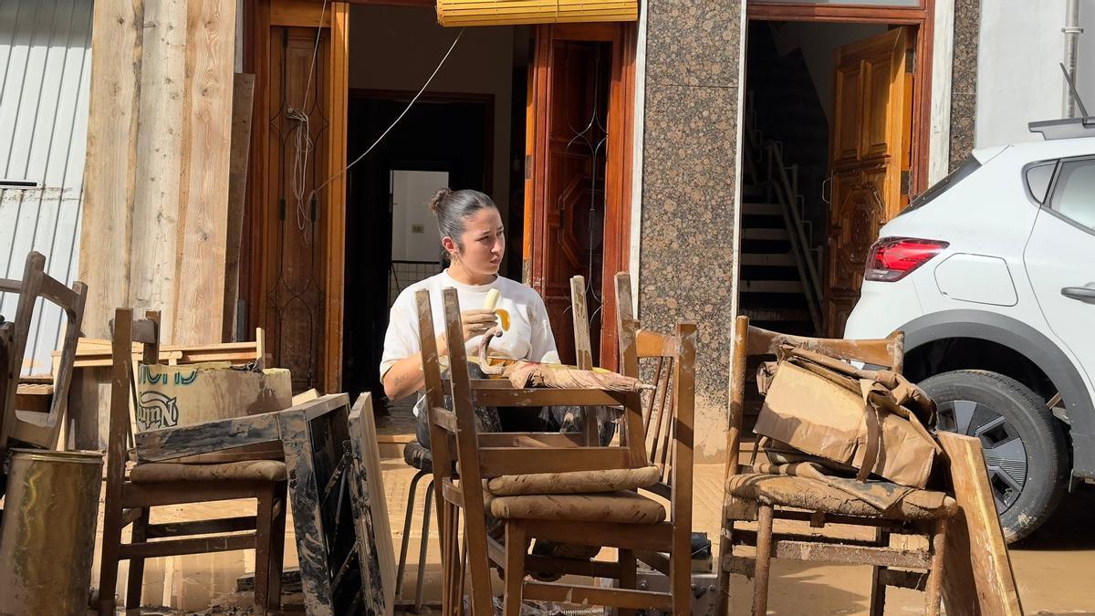 Una joven se come un plátano rodeada de muebles embarrados.