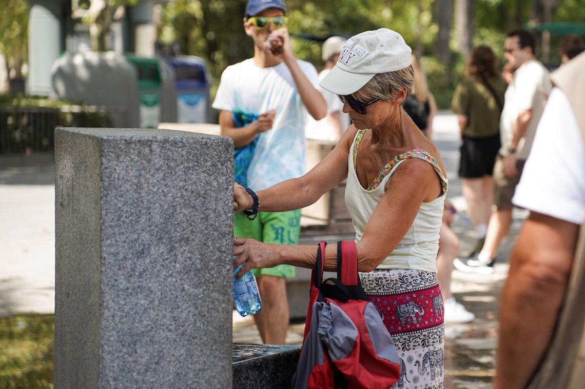 Personas bebiendo agua en una fuente pública de agua potable en Sevilla durante un día de calor