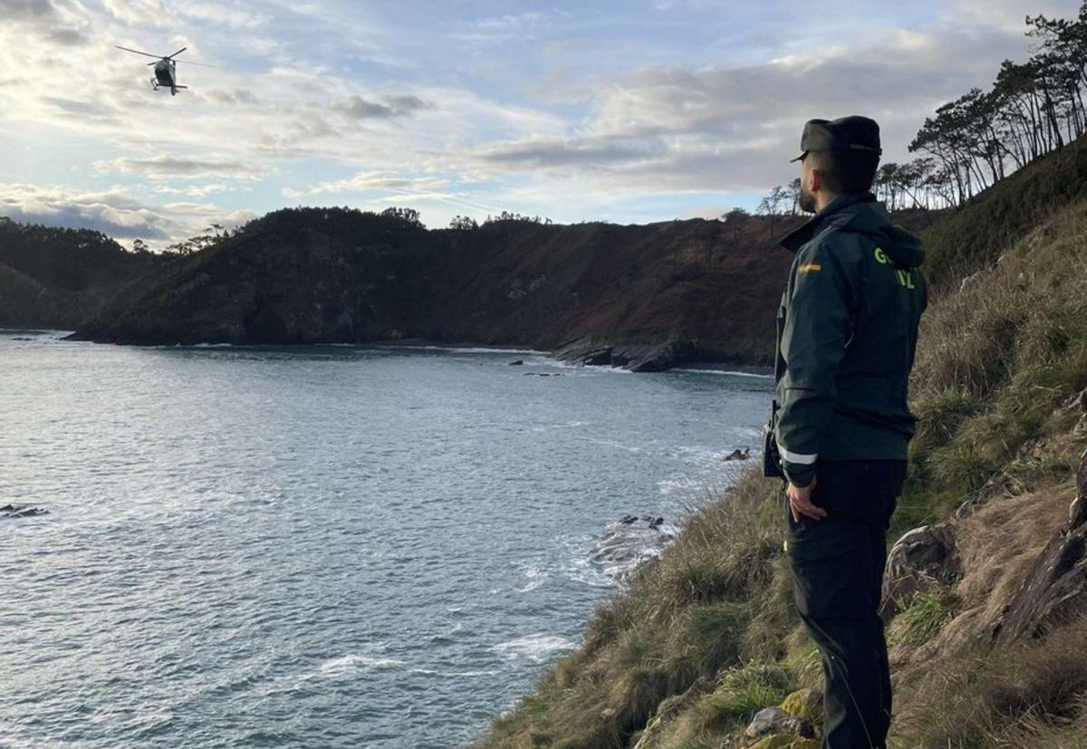 Un guardia civil observa la costa coañesa, con el helicóptero al fondo.