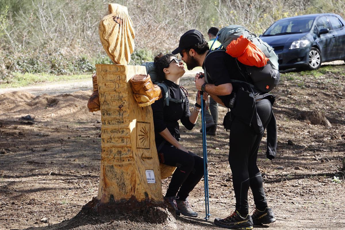 Dos peregrinos italianos utilizan el asiento de madera dedicado al Camiño.