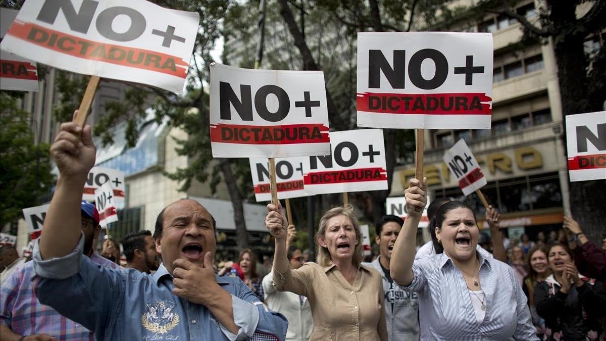 Manifestantes contrarios a Maduro sostienen pancartas en las que reclaman que se acabe la dictadura en Venezuela.