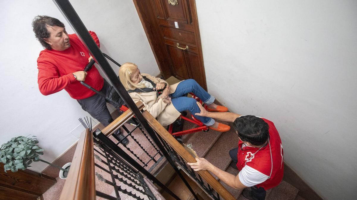 Bárbara Frau baja las escaleras de su casa en Palma con voluntarios de Cruz Roja.