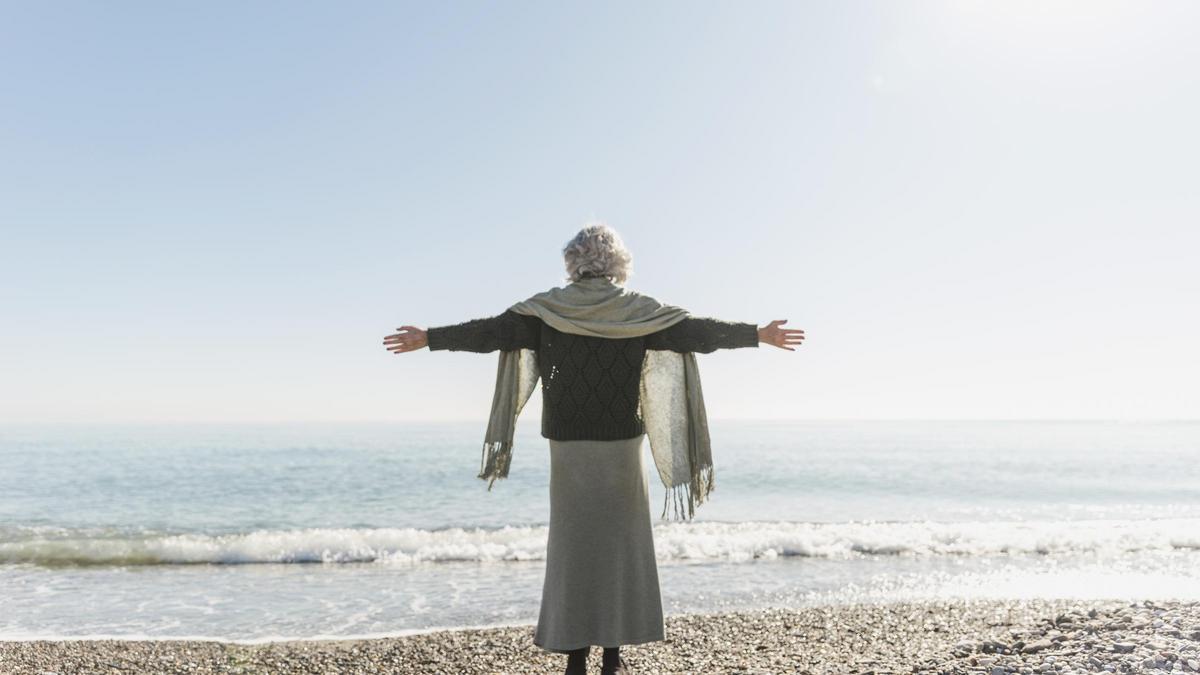 Una mujer mayor, de espaldas, mira hacia el mar.
