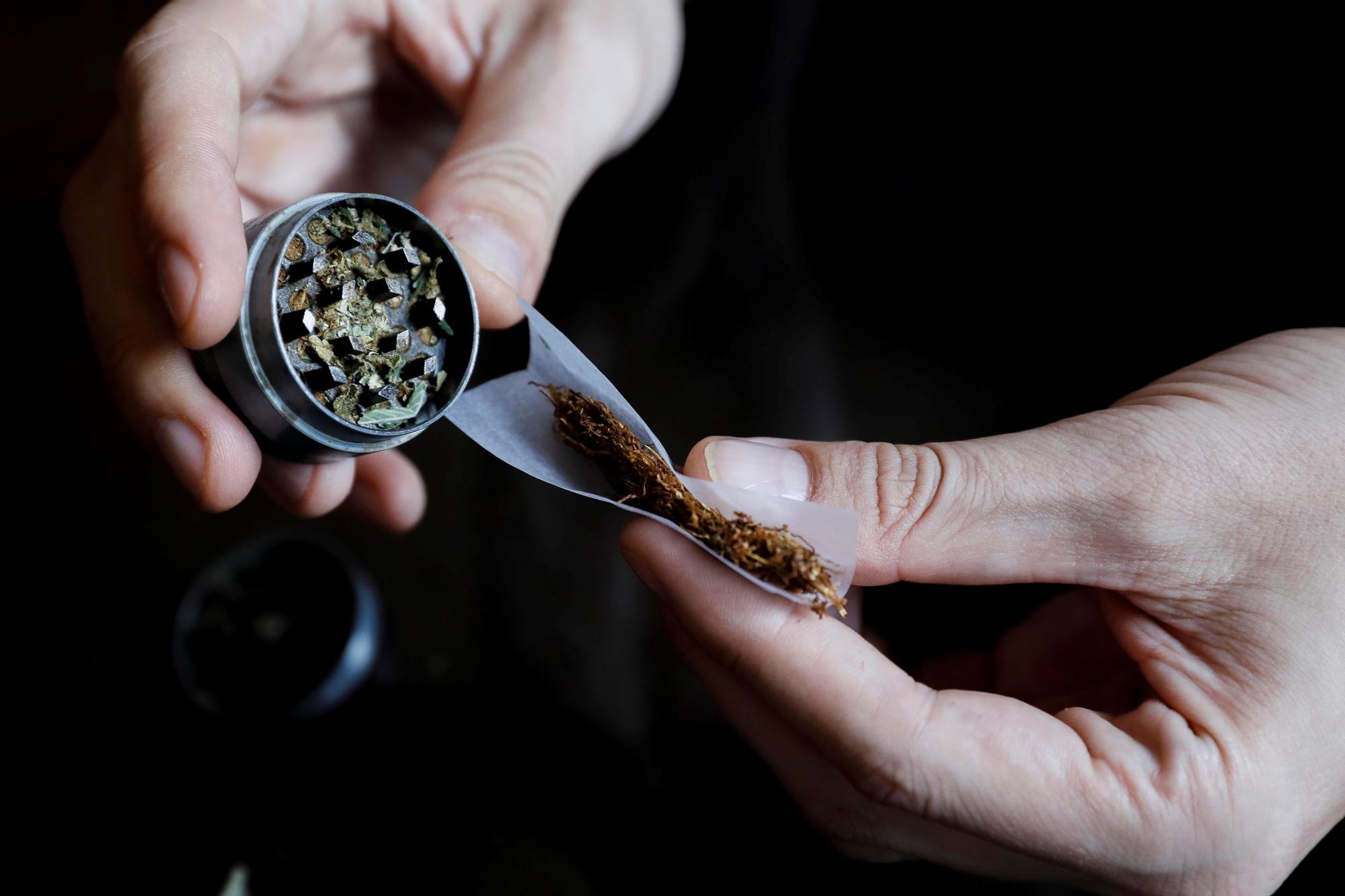 Una persona prepara un porro con marihuana.