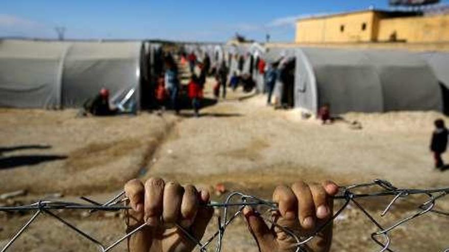 Manos en la alambrada de un campo de refugiados.