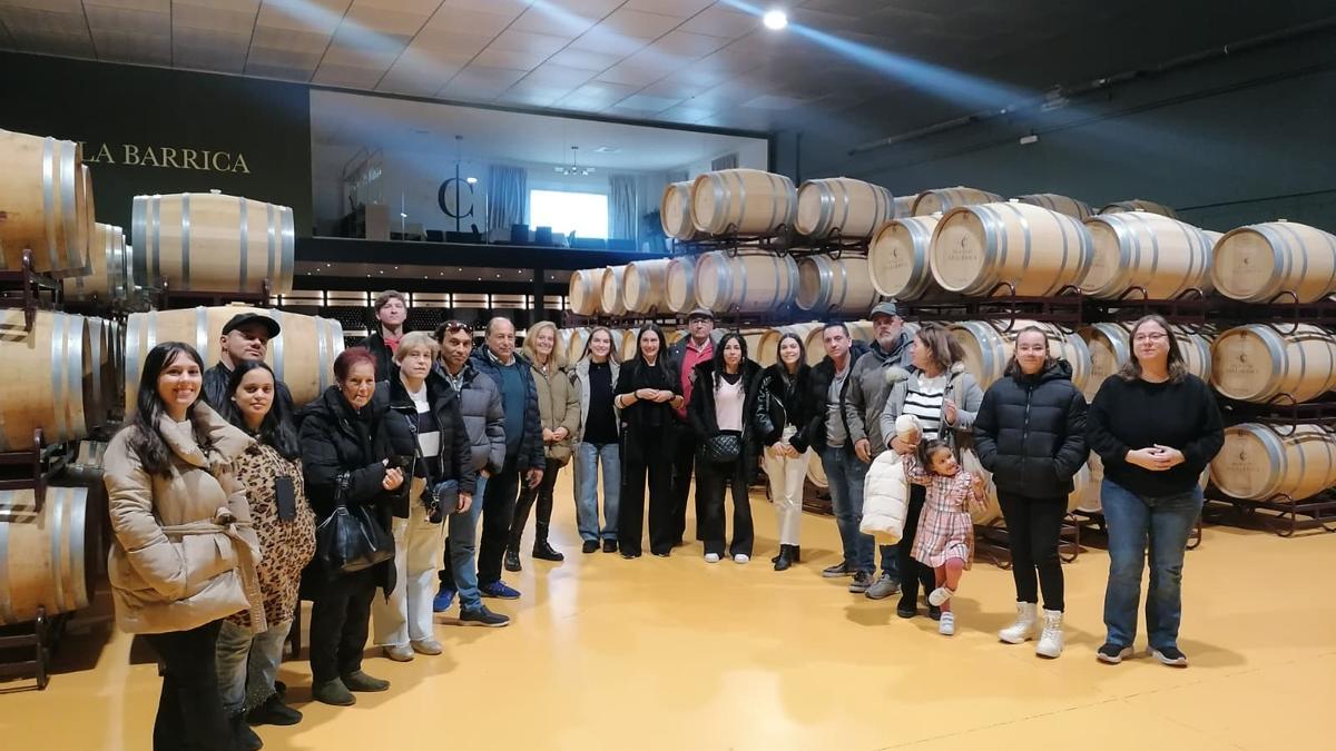 Participantes en la visita posan con responsables de la bodega y de la asociación en la nave de barricas.